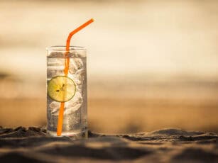 Glass of Gin Tonic with straw and lime slice on the beach, at su